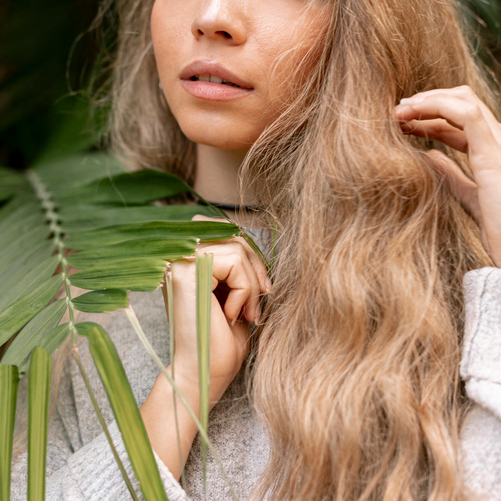 Mulher com cabelo solto e luminoso em ambiente natural, transmitindo beleza, suavidade e cuidado capilar de inspiração botânica.