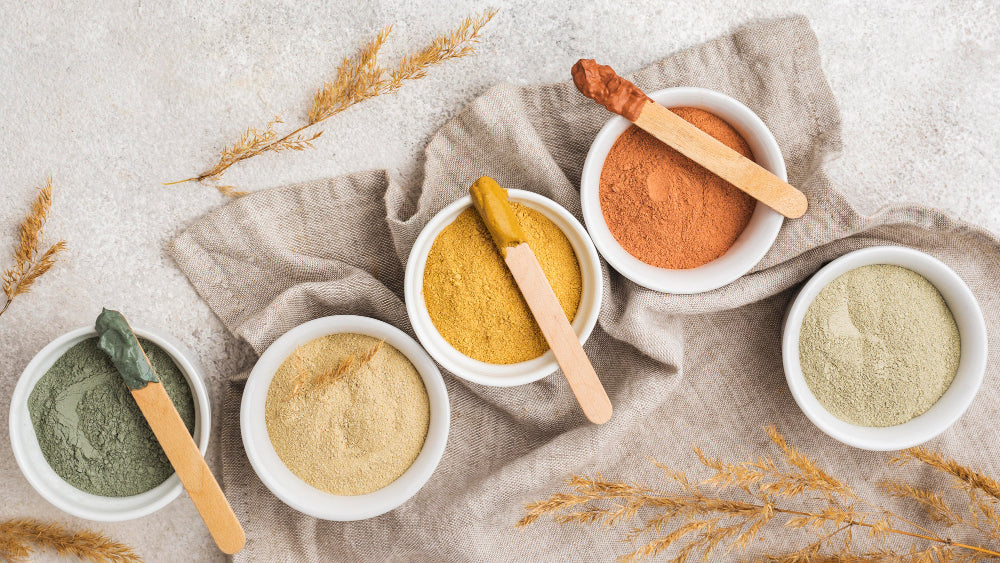 Taças com superalimentos em pó naturais como spirulina, maca e outros superfoods ricos em nutrientes sobre fundo neutro.