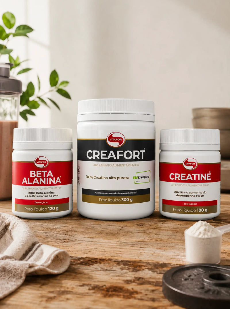 Suplementos Vitafor Beta Alanina, Creafort e Creatine sobre mesa de madeira, num cenário de treino com shaker, doseador e peso.